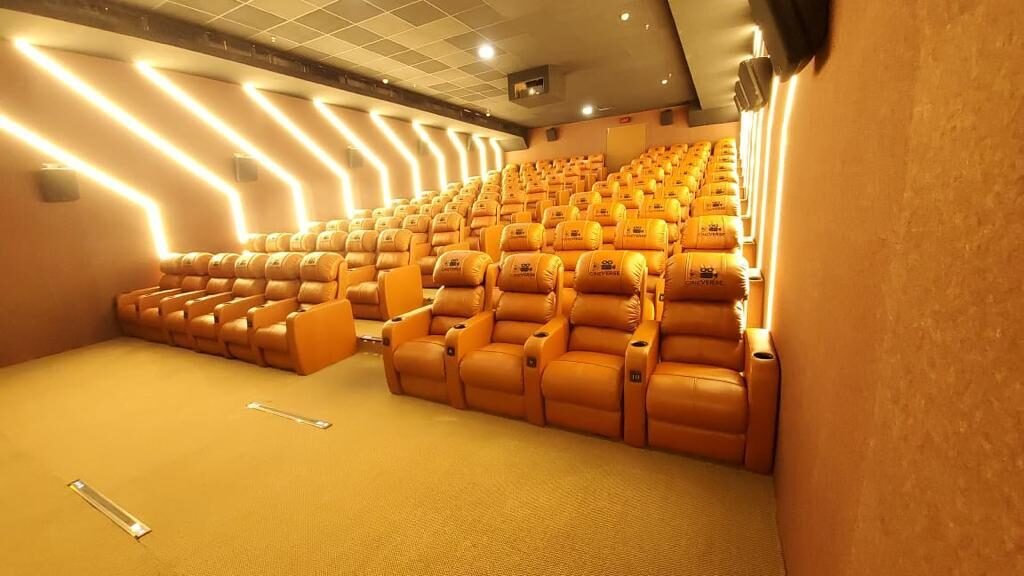 Tan leather recliners beneath gold chevron wall lighting in a Cineverse Multiplex auditorium